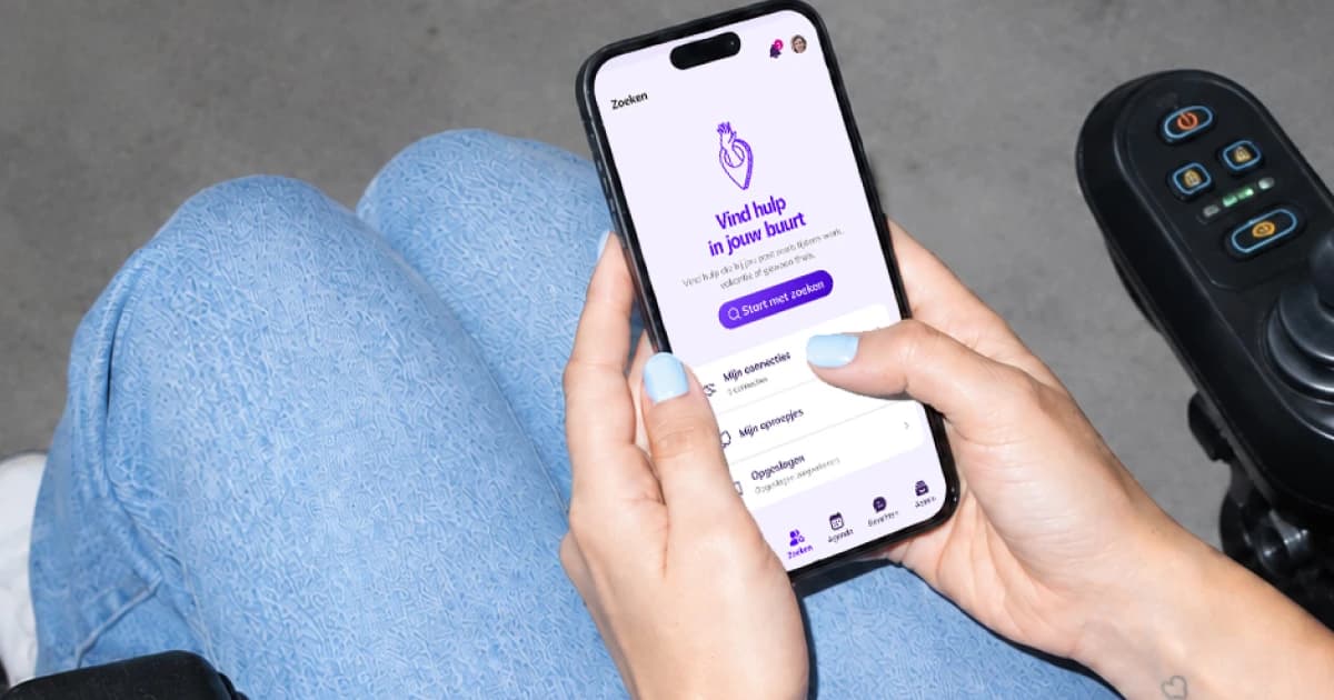 Iemand in een rolstoel houdt een telefoon vast met het zoekscherm van de Carepool-app: vind hulp in jouw buurt.