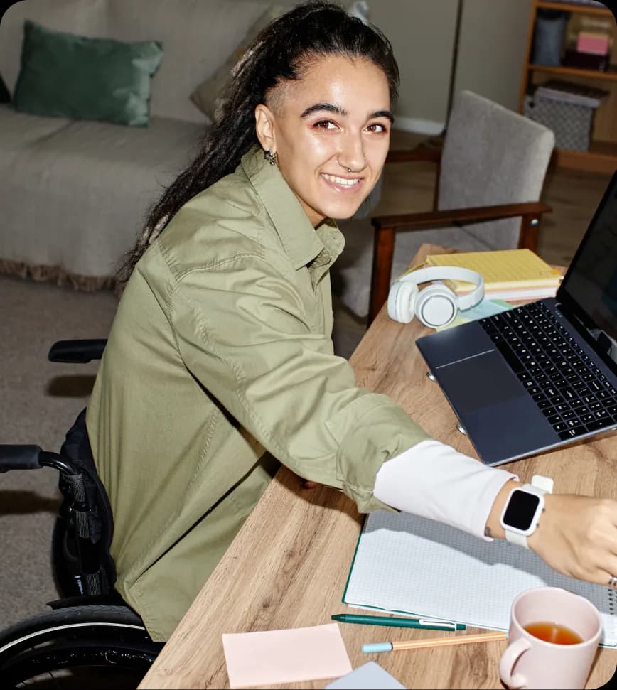 Iemand in een rolstoel werkt lachend achter een laptop.